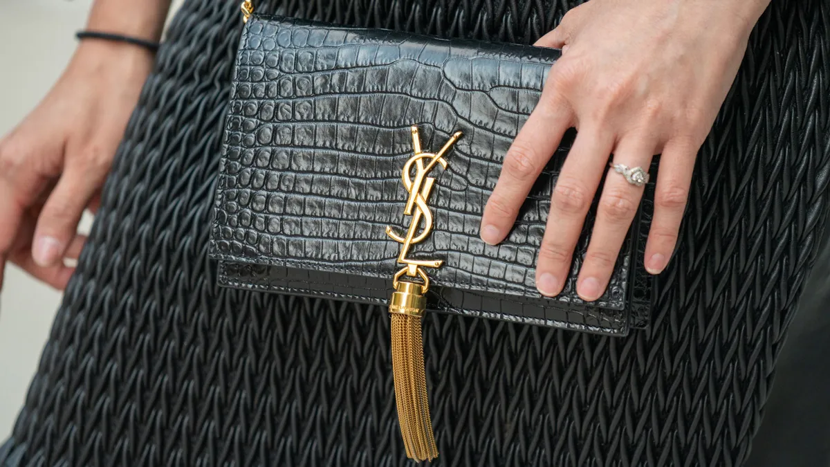 A person carries a black YSL monogram bag with gold hardware and a gold tassel.