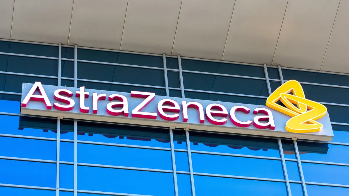 A sign reads "AstraZeneca" with the company logo on an all-glass-grided building facade. 
