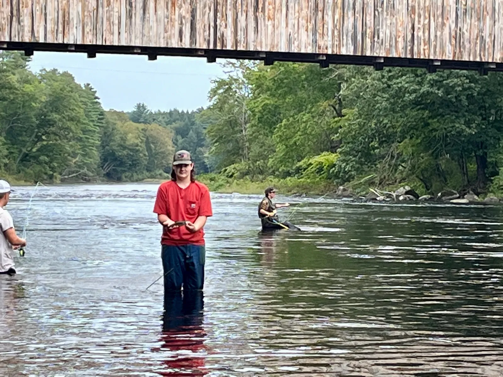 A student stands knee-high in a waterway holding a fish.