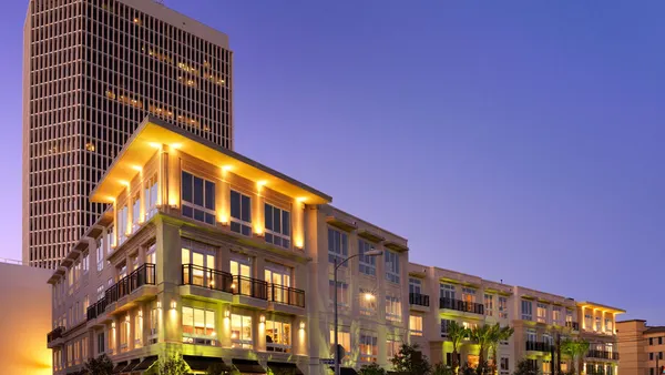Four-level apartment property with palm trees in the foreground and a high-rise in the background