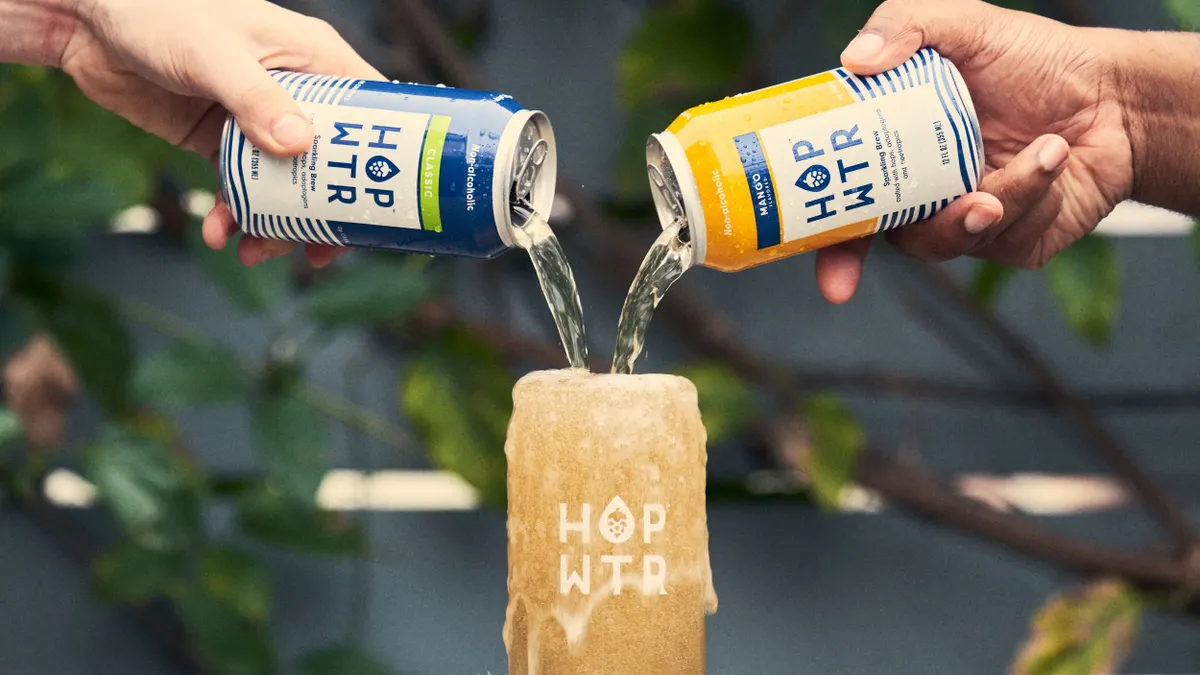 Two cans of hop water pour and overflow into a glass.