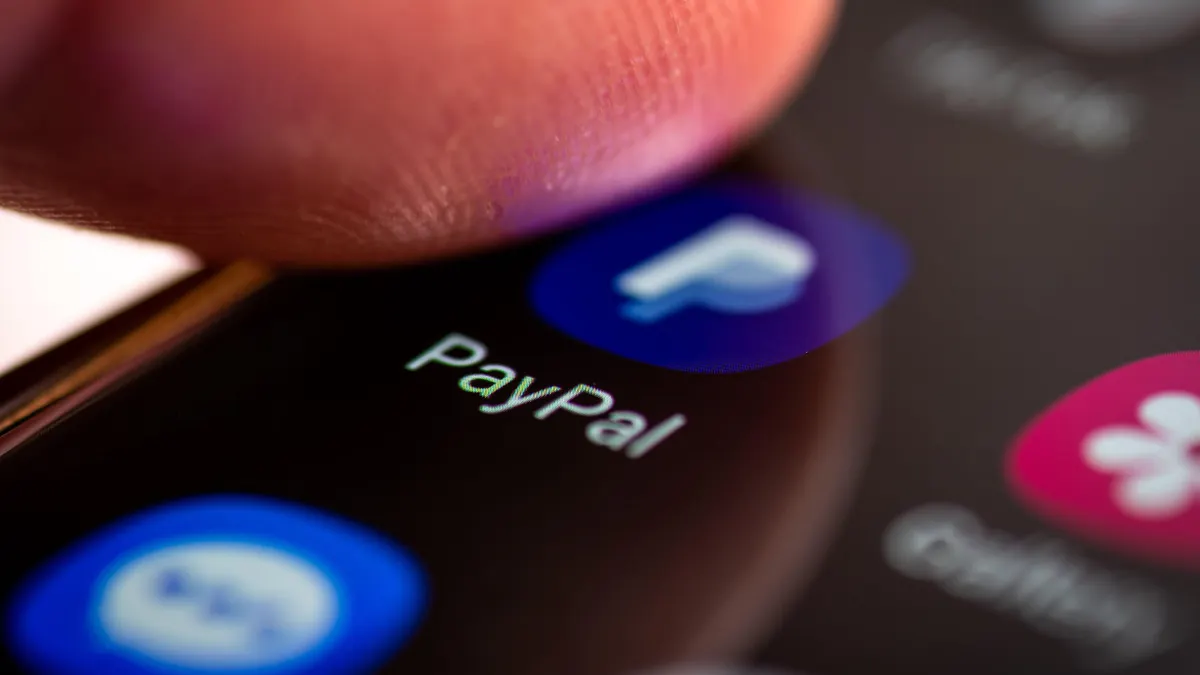 Close-up of an Android smartphone screen displaying the PayPal app icon and name, with a fingertip poised above the screen, indicating user interaction.