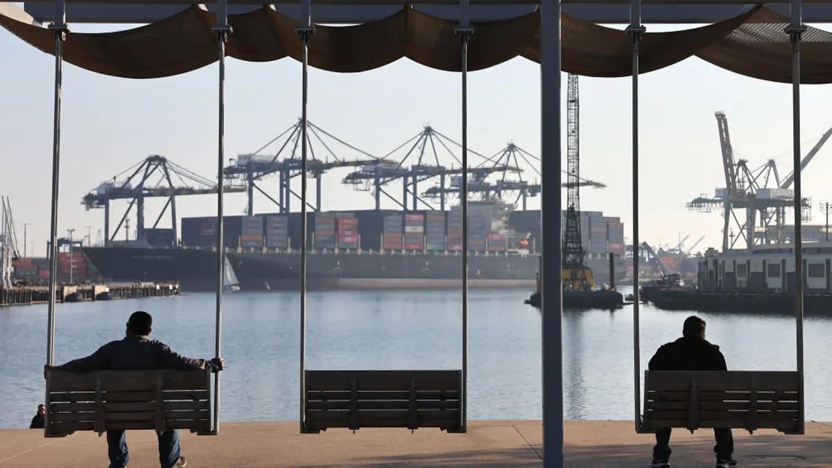 People sit at a park near shipping containers stacked on a container ship at the Port of Los Angeles on December 4, 2024 in Wilmington, California.
