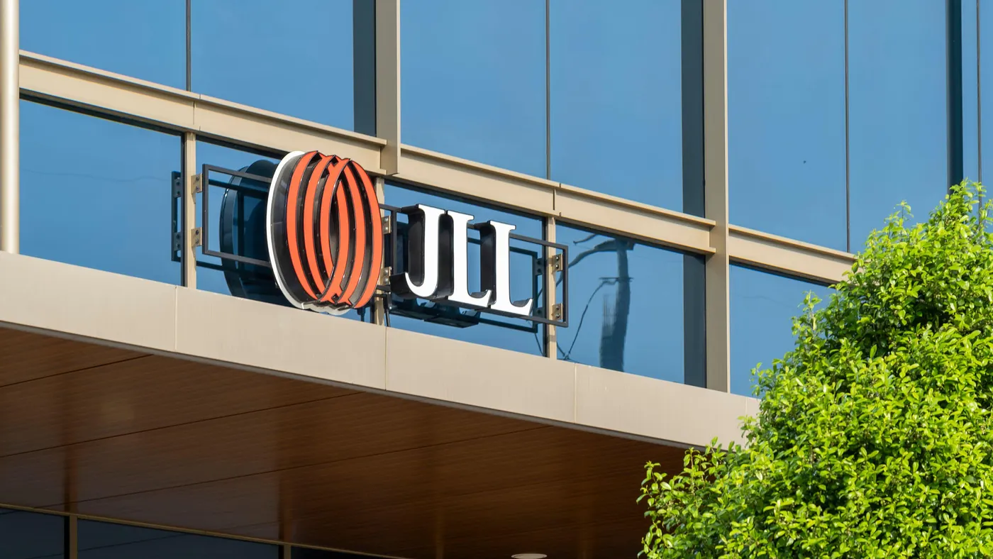 A facade of a glass sleek building with a large logo of "JLL" with a tree tot he right. 