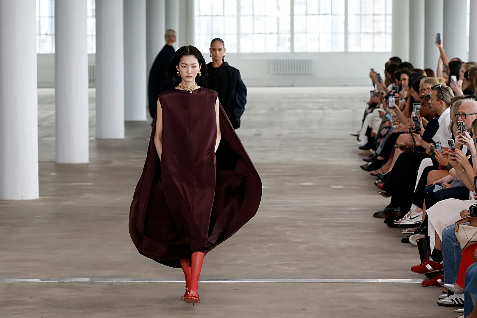 A model in a cape-like dress walks down a runway.