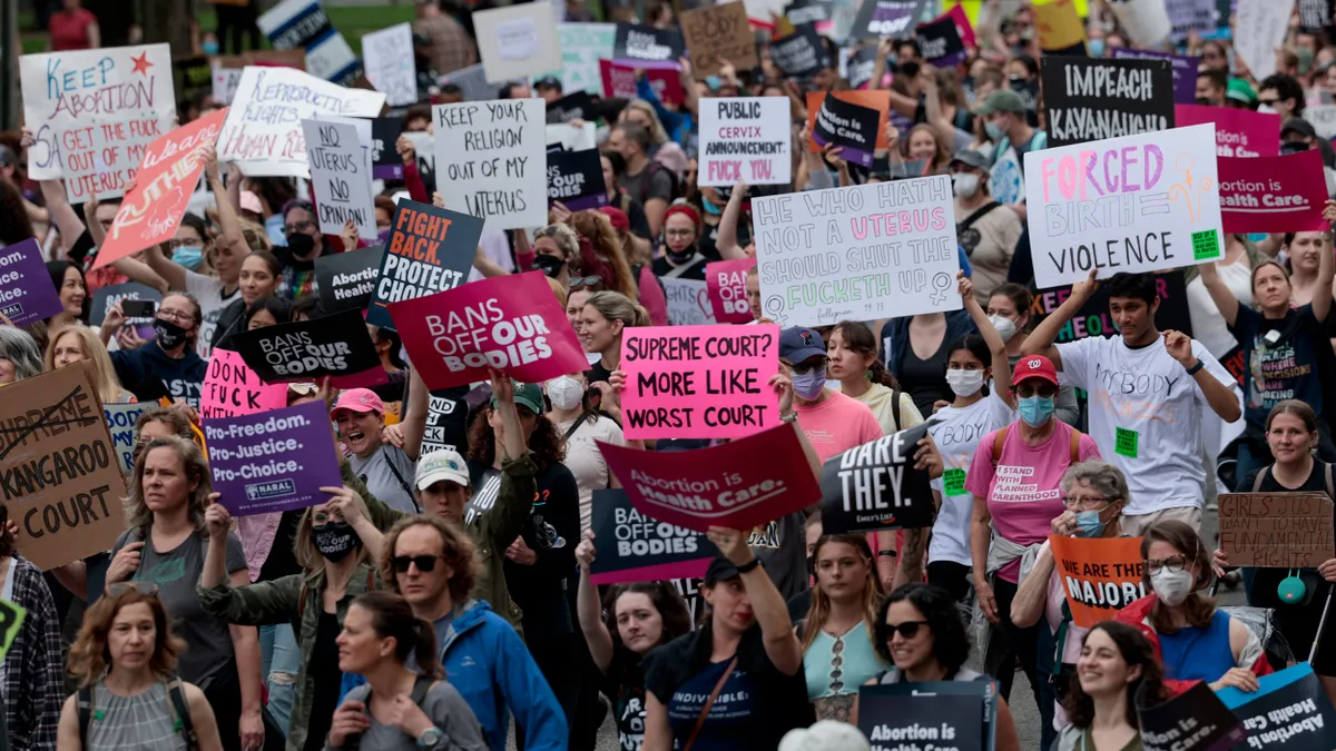 A large group of protestors gather on the street. Some signs read "bans off our bodies", "Forced birth = violence", and "fight back. protect choice."