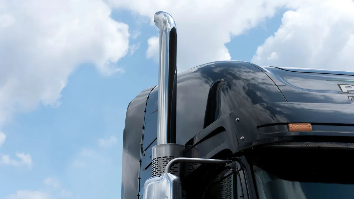 A tractor's exhaust pipe with blue sky and white clouds in the background.