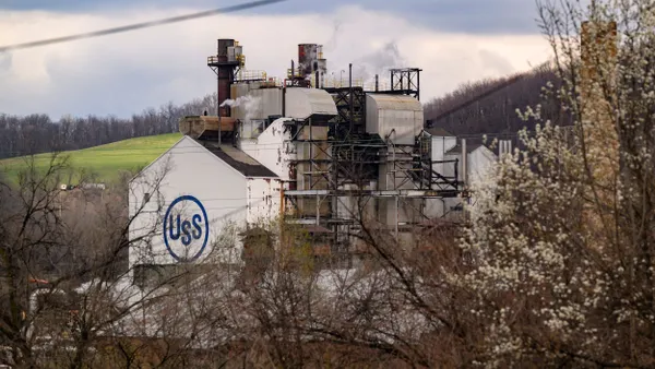 A white building with the blue U.S. Steel logo on it, attached to an exterior plant.