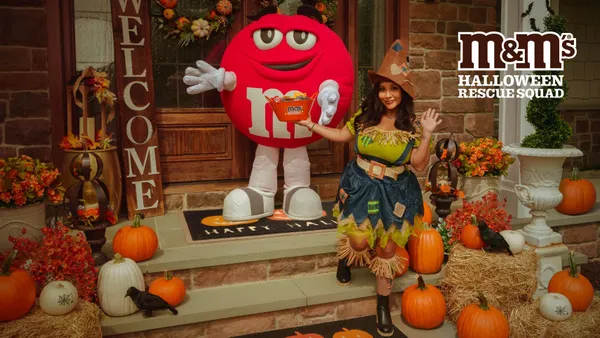 Snooki, dressed as a scarecrow, stands on a decorated front stoop with someone in a red M&Ms costume.