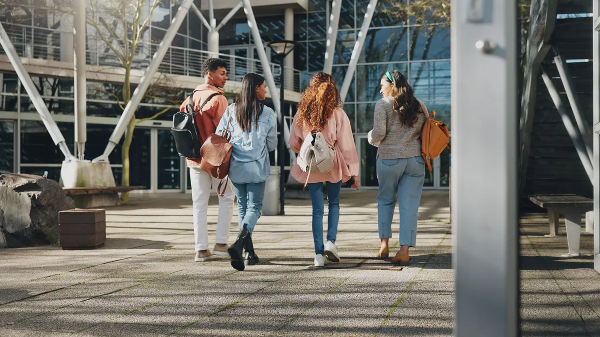 A group of students walk together on a sidewalk on a college campus.