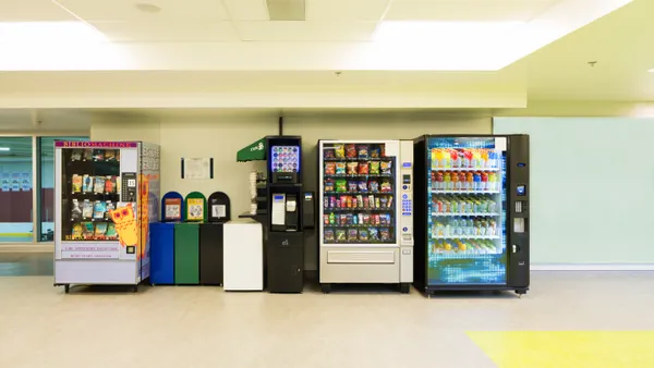 Various vending machines and trash cans lined up against a wall.