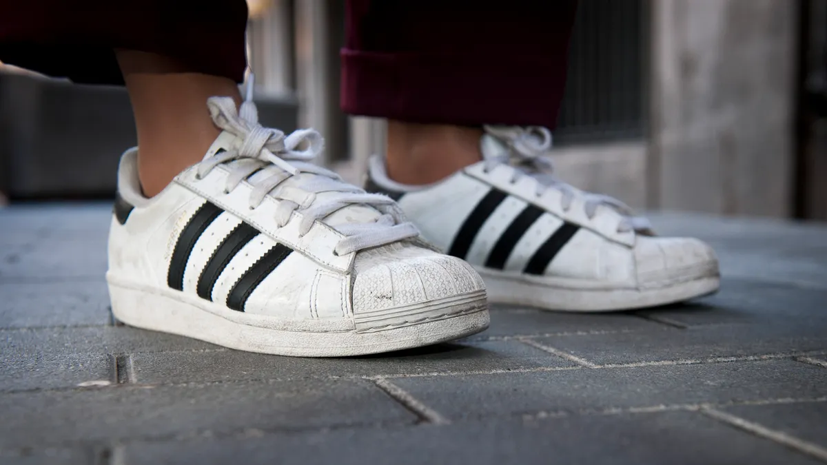 A closeup of a person's shoes, white Adidas sneakers with black stripes.