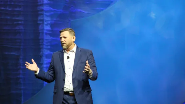 A picture of a man in a suit delivering a speech in front of a blue background.