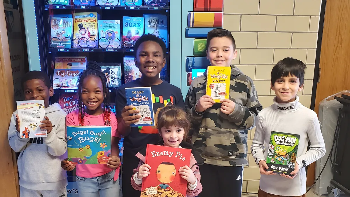 A diverse group of elementary school students poses in front of a book vending machine.