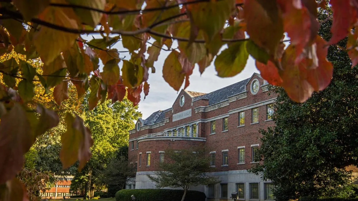 A brick academic building on a sunny day with fall leaves in the foreground.