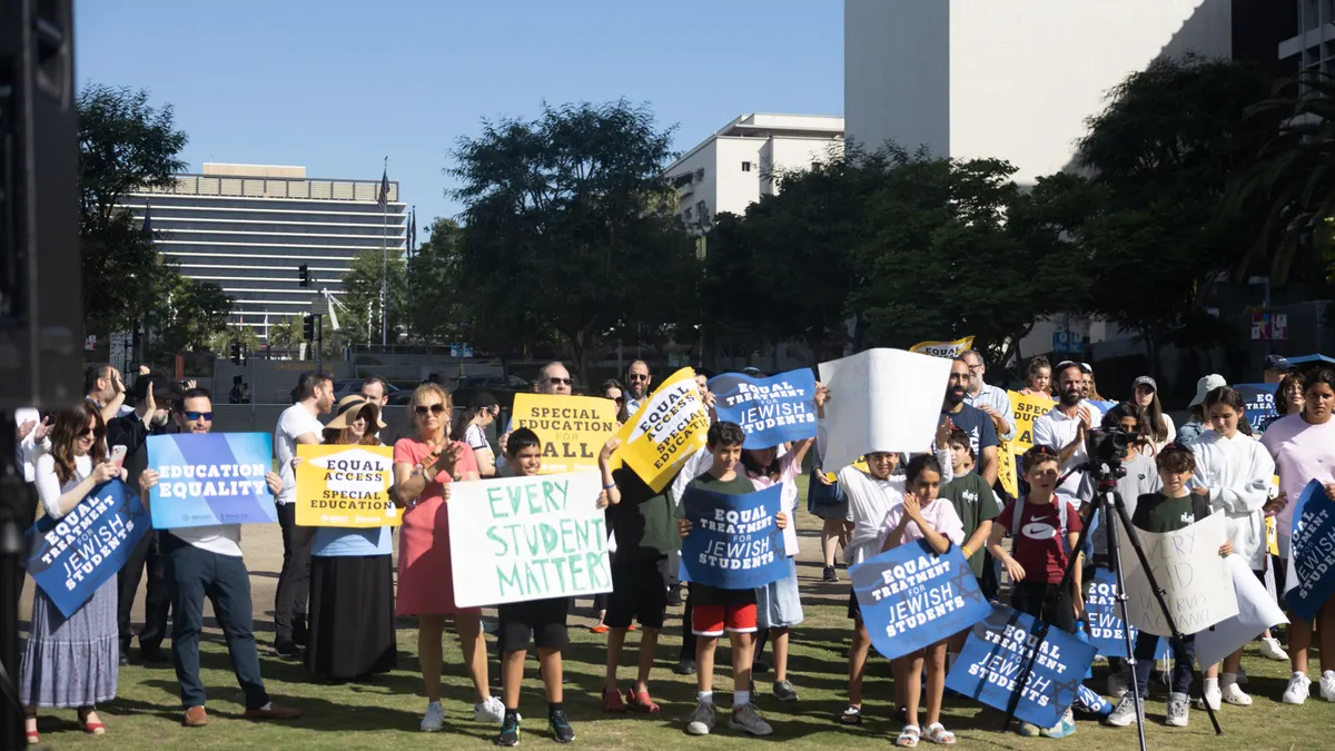 A group of students and adults are standing outside and are holding posters with wording.