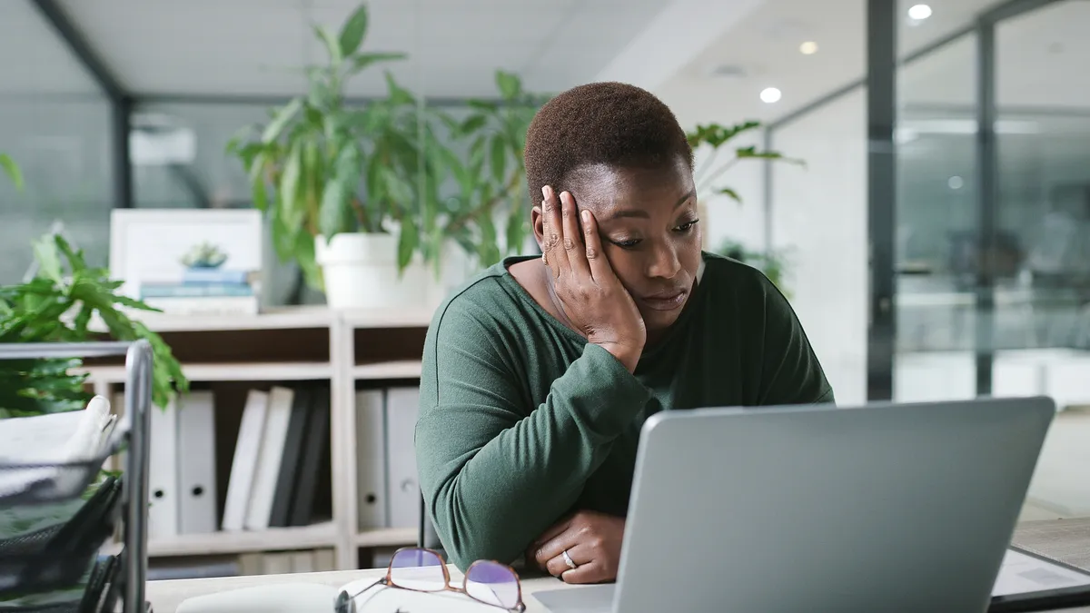 Woman in front of laptop at desk looking burned out and exasperated.