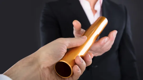 a Close-up photo Of A Businessperson Passing Golden Relay Baton To a Colleague.