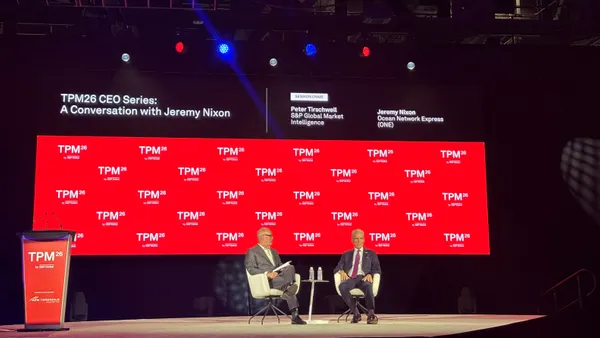 Two panelists sit in front of a red background.