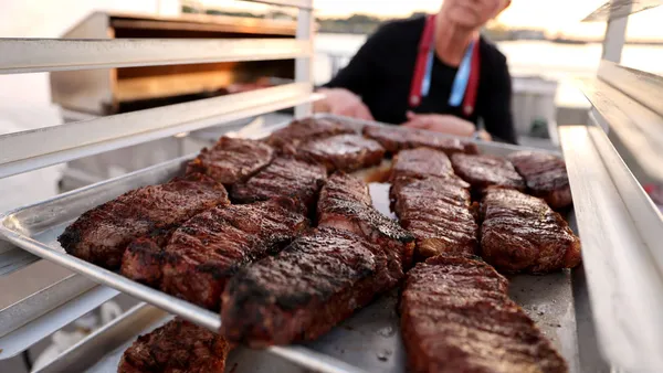 A woman pulls steak out of an industrial grill