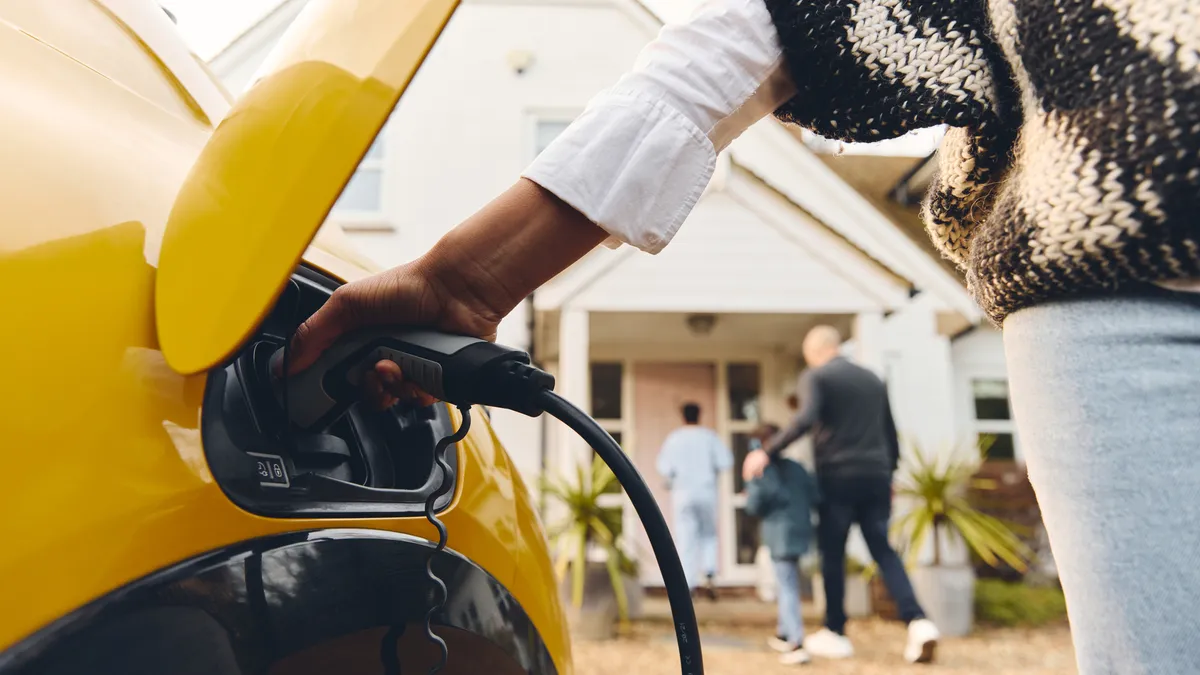 A person is holding an electric vehicle charging plug into a yellow EV.