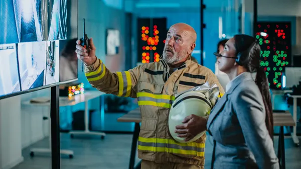 Two emergency service controllers look at live camera feeds for a building.