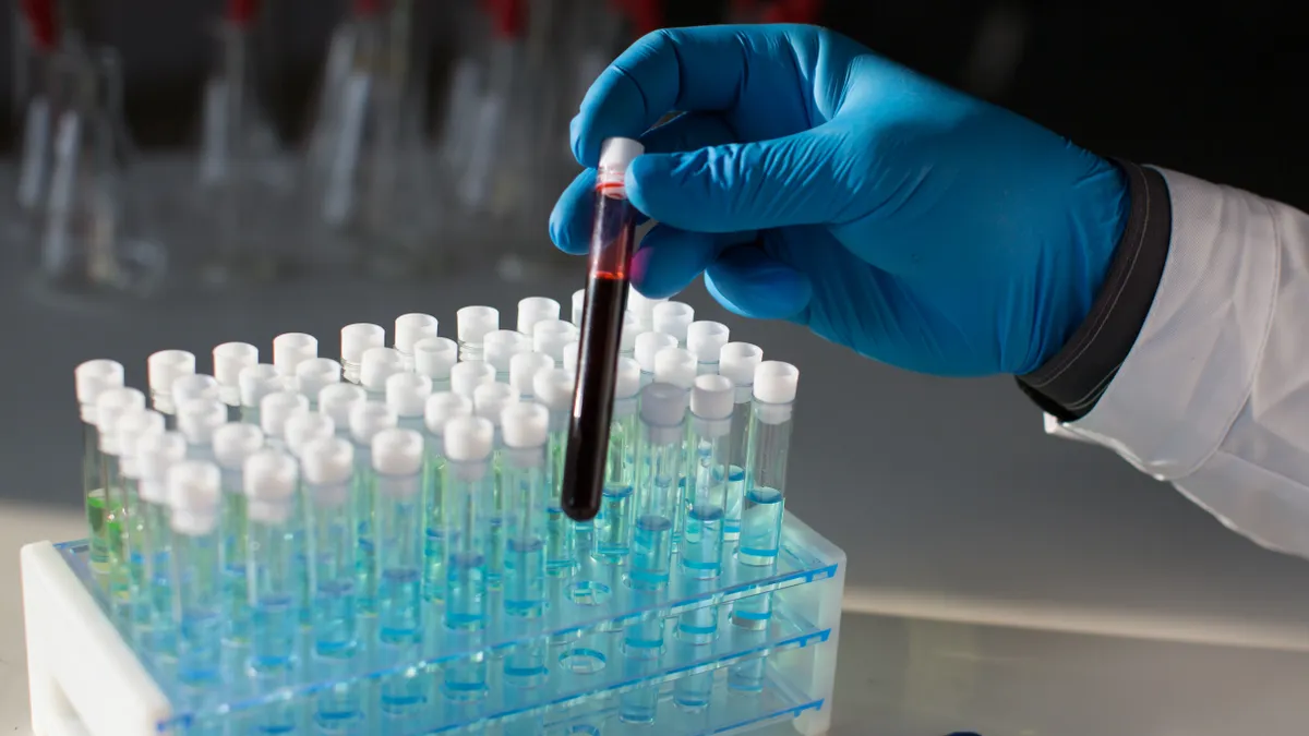 A person wearing a blue glove holds a test tube with red liquid