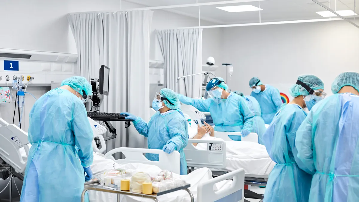 Healthcare workers wearing blue scrubs assisting patients in hospital beds.