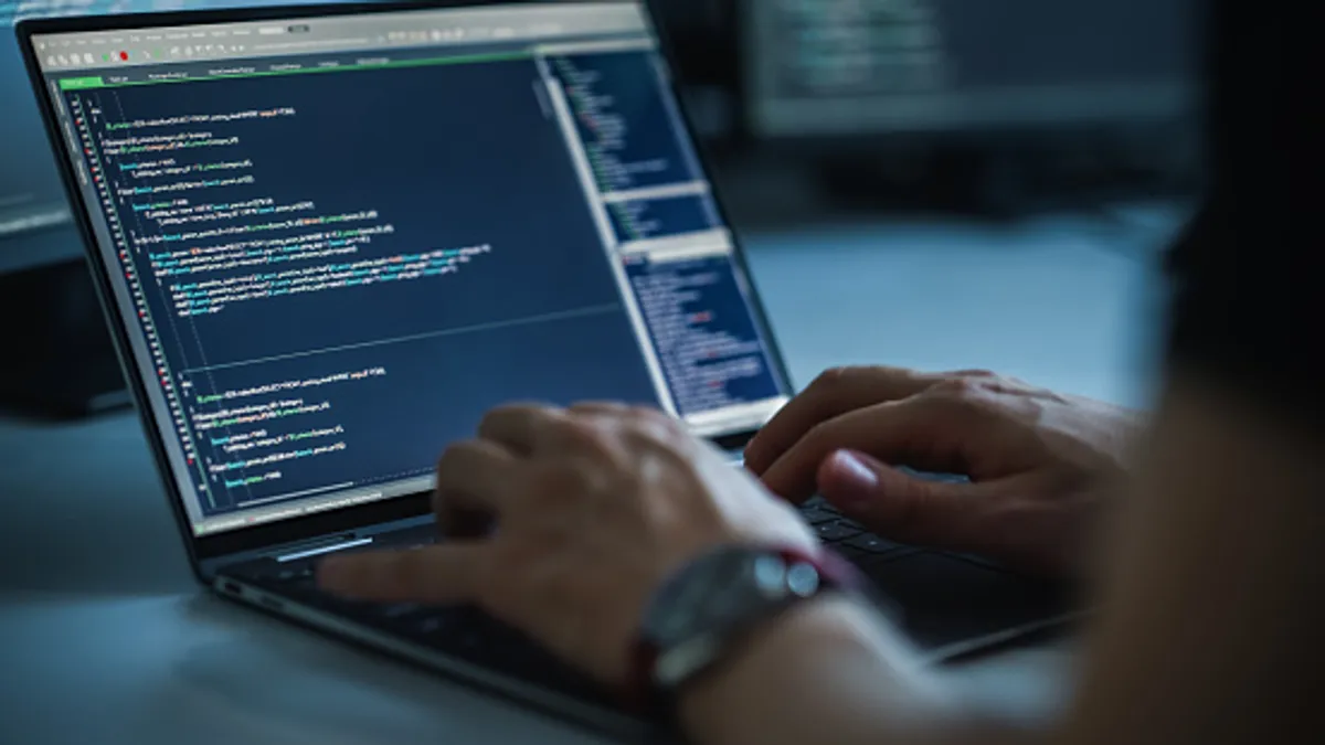 Close-up focus on person's hands typing on a computer keyboard while screen shows coding language user interface.