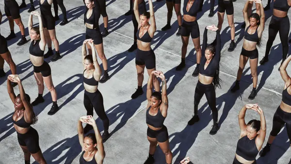 A group of people stand evenly spaced apart stretching on a gray ground.