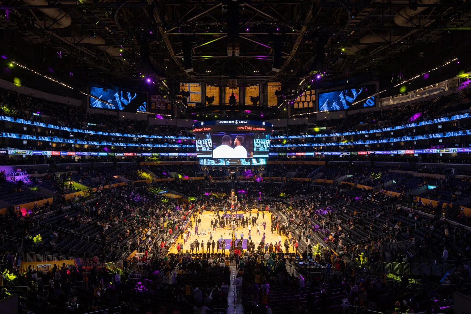 An elevated view of a basketball arena as players and fans file in.