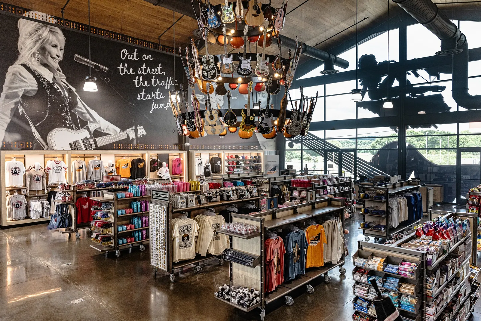 A photo looking down from the second floor of a store into a shop on the first floor. A chandelier with guitars all over it hangs over racks and shelves of merchandise.