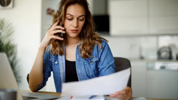 A woman on the phone while looking at a piece of paper.