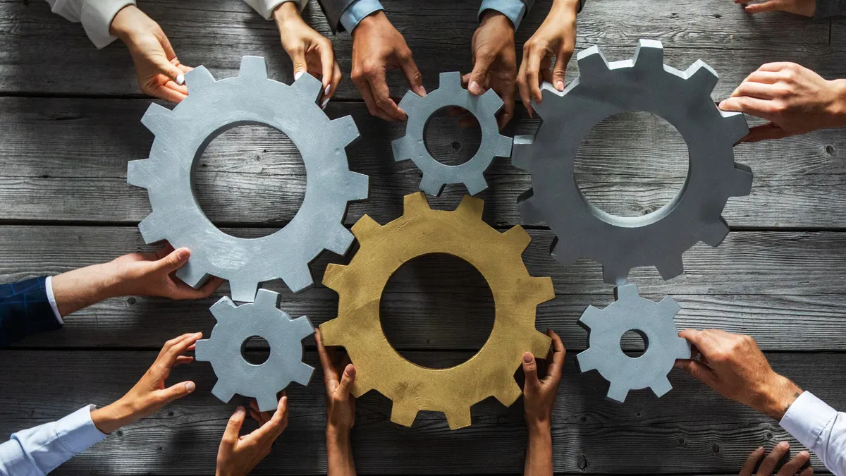 Group of business people joining together silver and golden colored gears on table at workplace top view