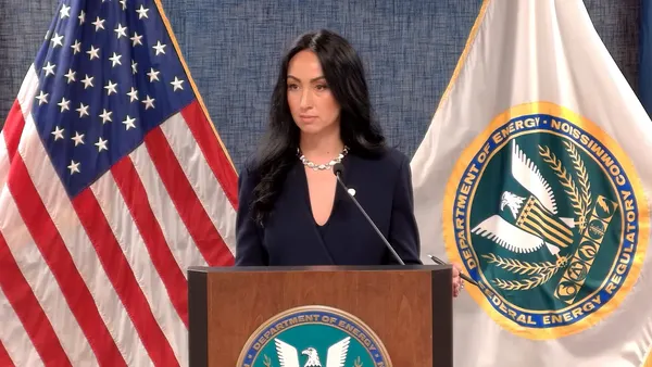 A woman stands at a podium if front of a US flag and a Federal Energy Regulatory Commission flag.