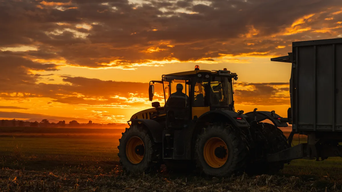 Farmer drives his tractor in the sunset over a crop field.