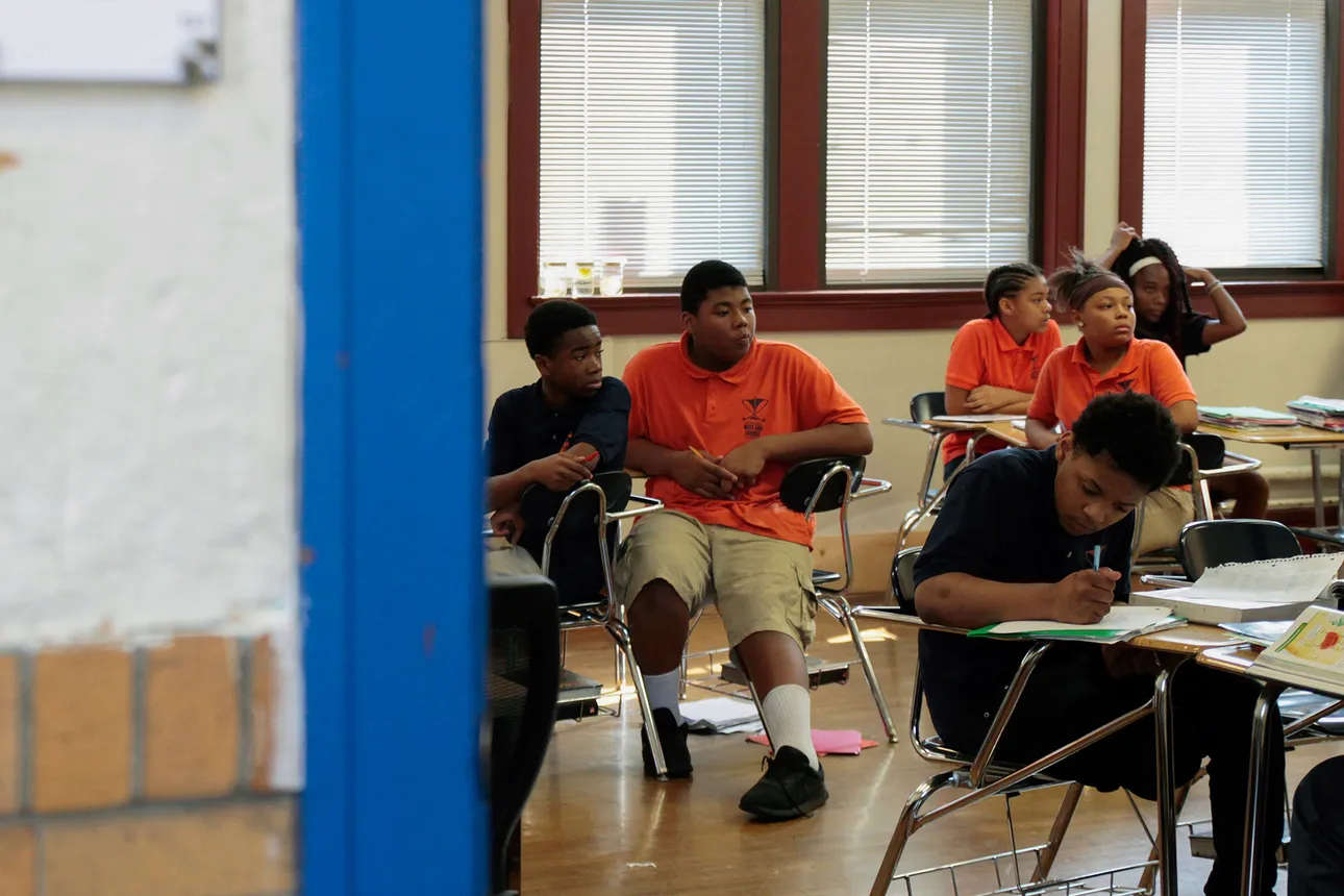 Black students wearing orange and Black uniforms sit in a classroom