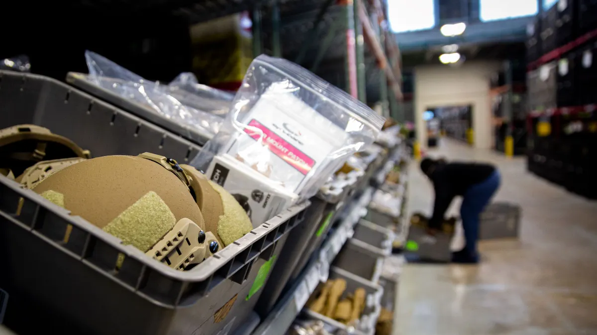 Tan helmets sit in a gray plastic container on a shelf.