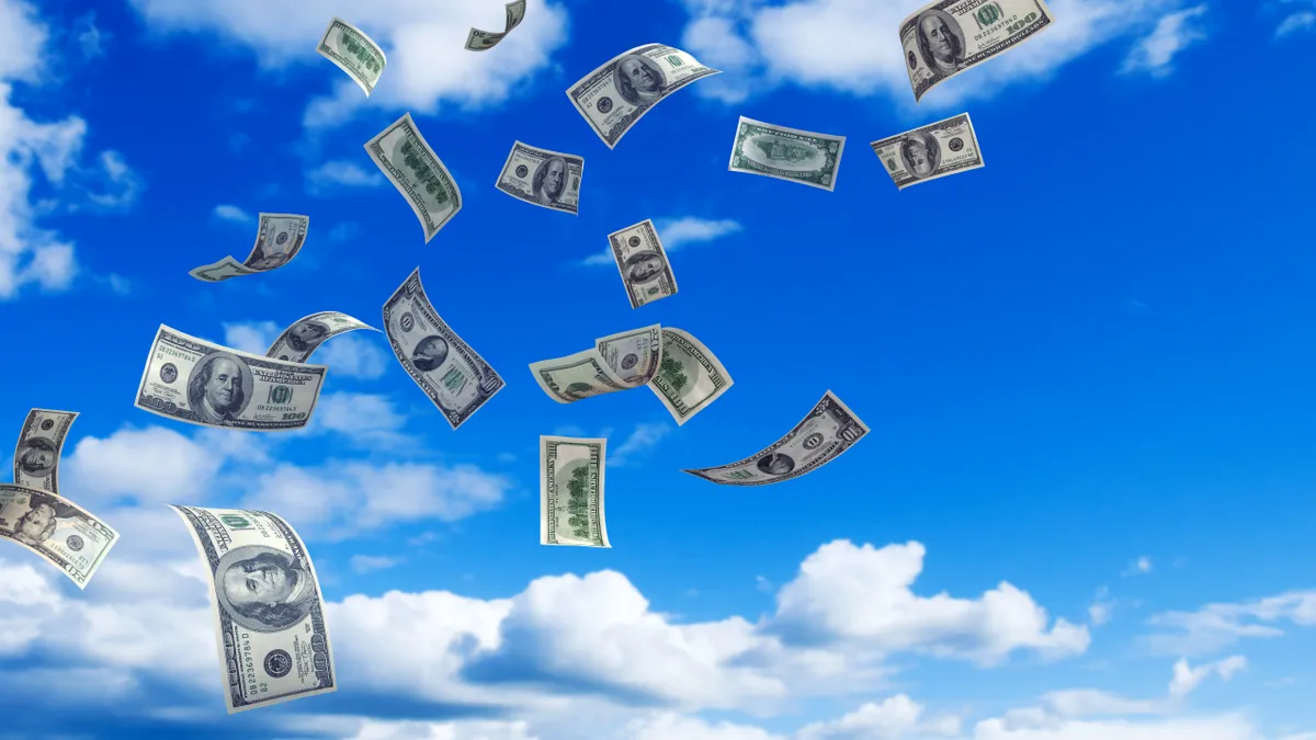 Hundred dollar bills being blow by wind in cloud-filled sky.