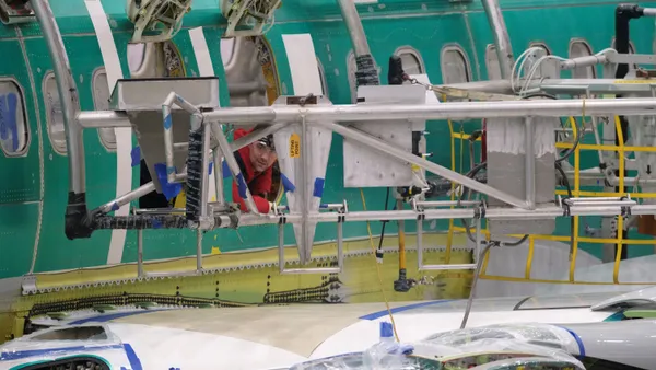 A person wearing orange protective gear peaking out of a plane window in a factory.