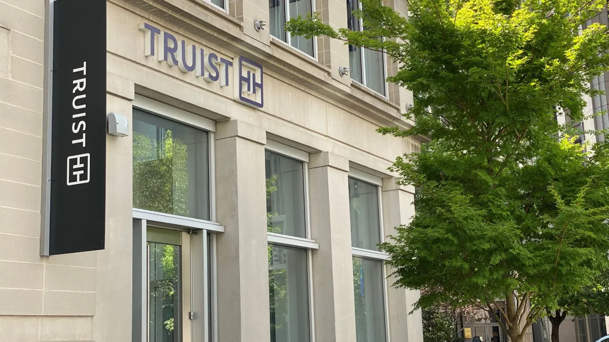 The Truist name is shown vertically and horizontally on a building facade with tree branches on the right side of the frame