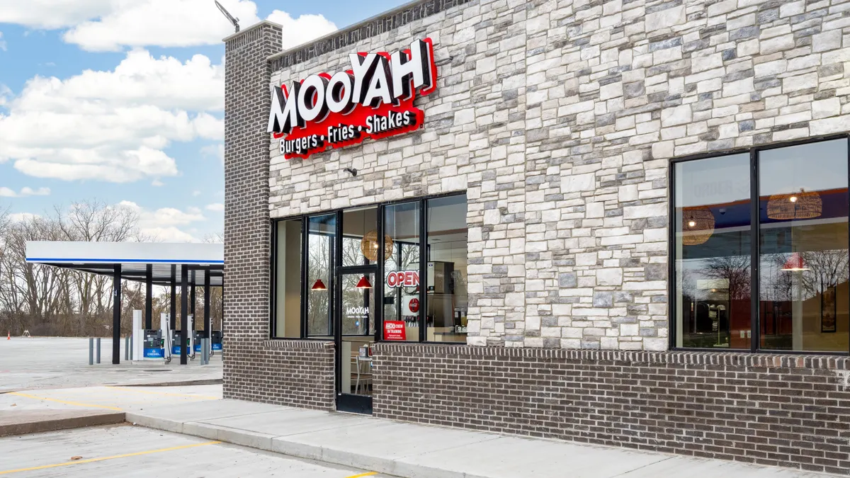 A photo of the exterior of a building adjacent to gas pumps. A Sign over the door says Mooyah Burgers, Fries, Shakes