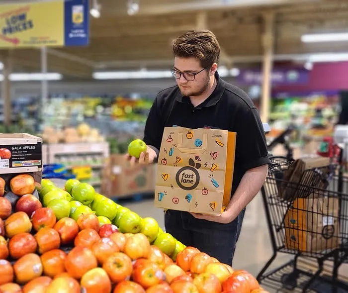 A person holds a bag that says "Fast Lane" in one hand and a green apple in the other hand.