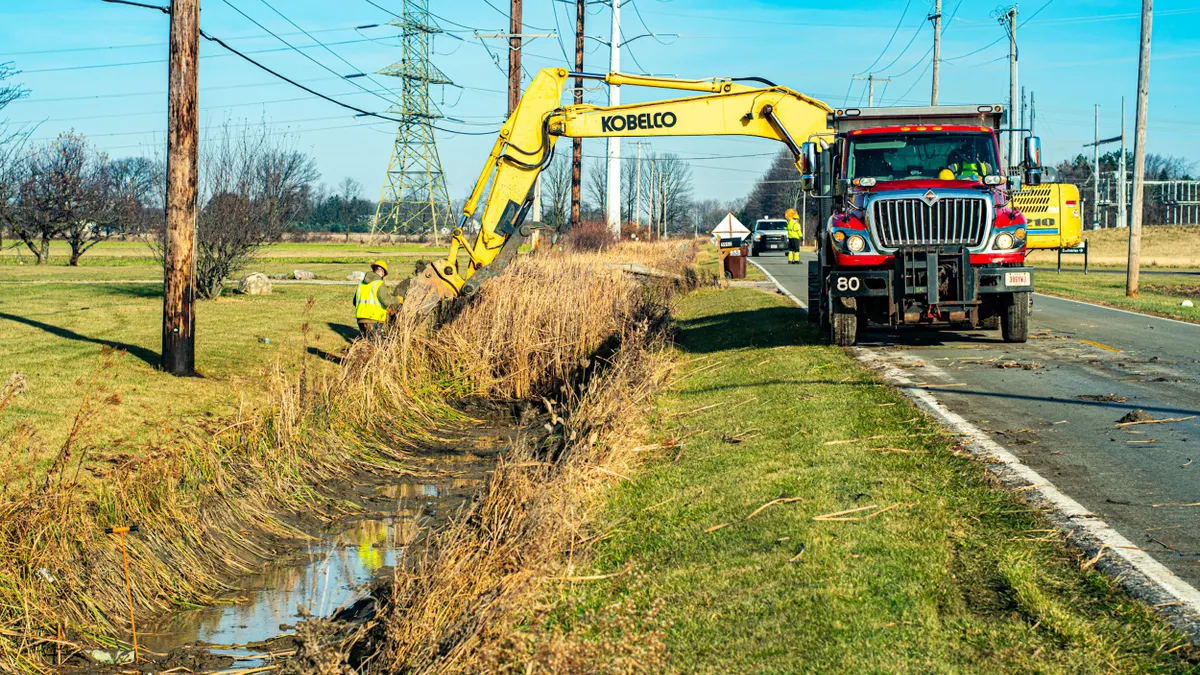 Worker and truck with crane along a ditch.