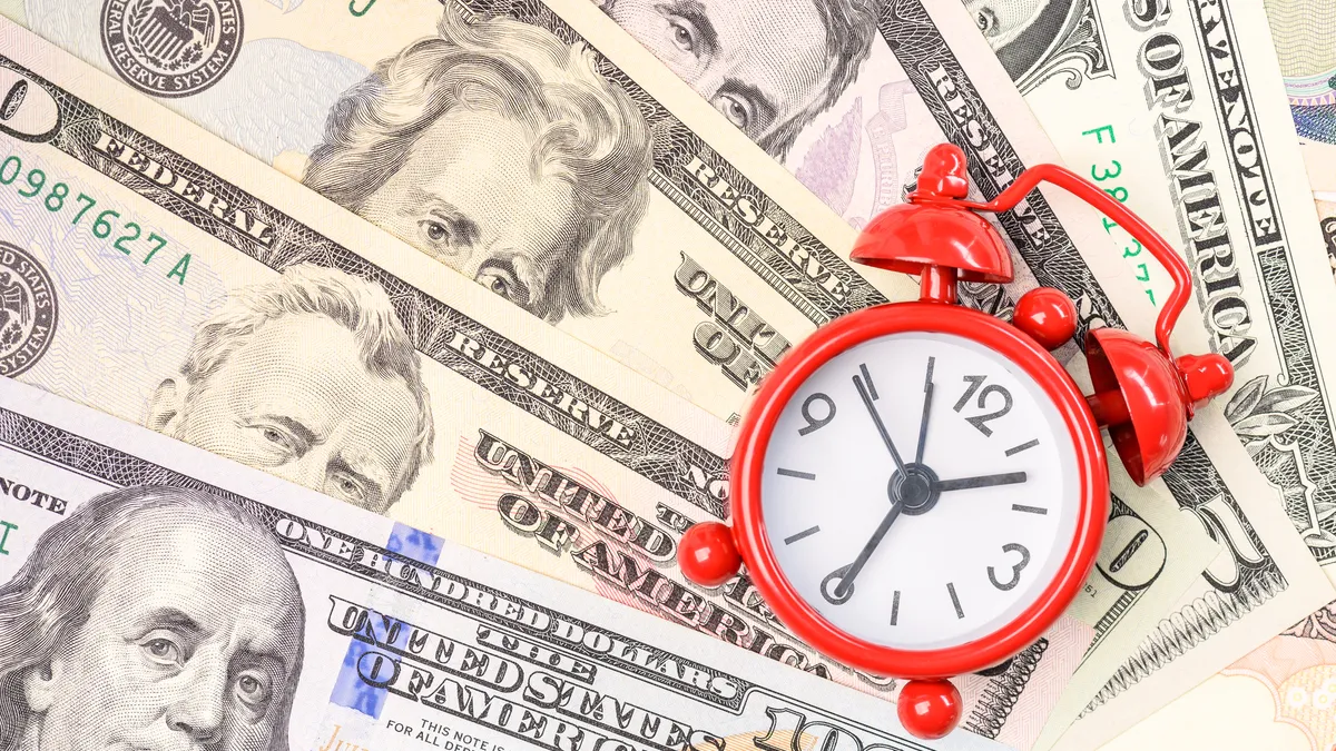 Time value of money concept : Red analog clock on US dollar banknotes, depicting receiving money today can be poised to increase the future value by investing and gaining interest over a period of tim