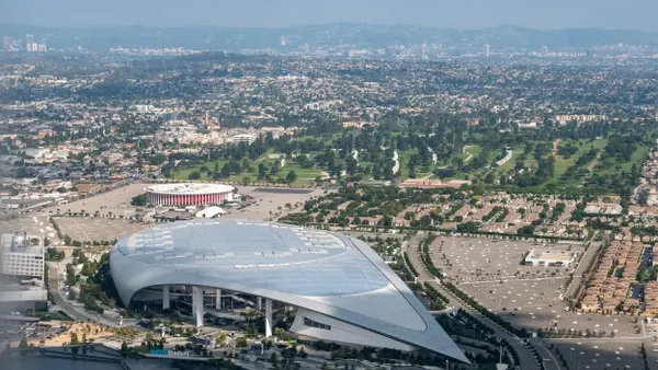 Aerial view of a large, low round stadium structure with a point at one end. Homes surround the stadium in the background.