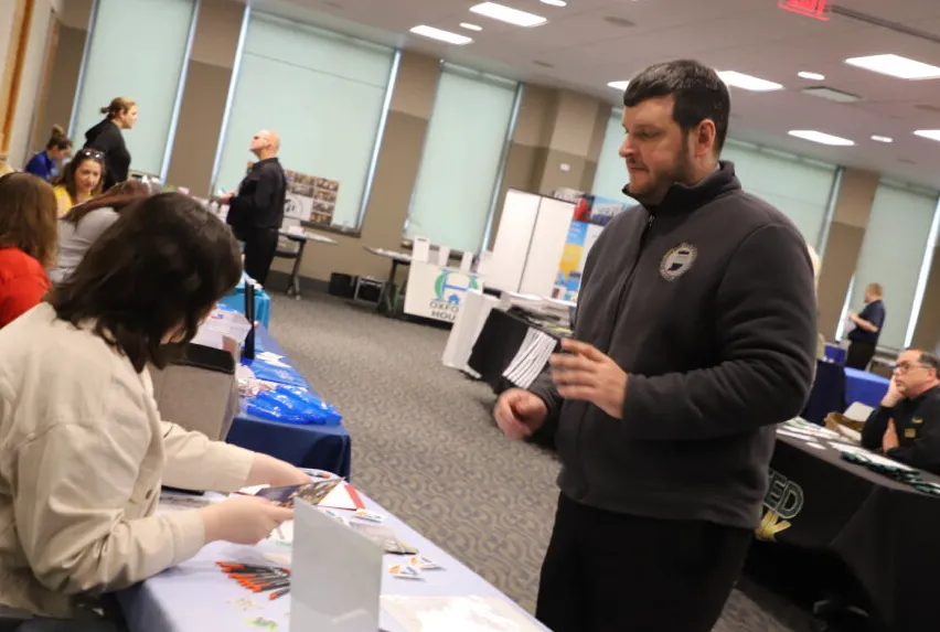 A person stands near tables set up in a room as part of a resource fair.