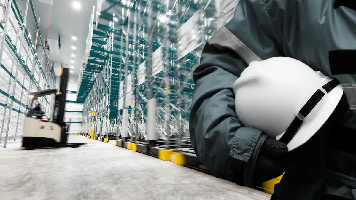 Safety hardhat for dangerous accident protection in warehouse during work. Cold room storage and freezing warehouse with stacker truck inside moving.