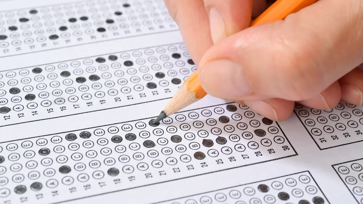 A hand is holding a pencil that is shading in bubbles on a test sheet