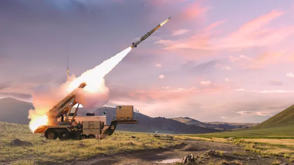 Smoke emitting from a missile shot out from a ground-based mobile launching station under a mostly cloudy and dusky sky.